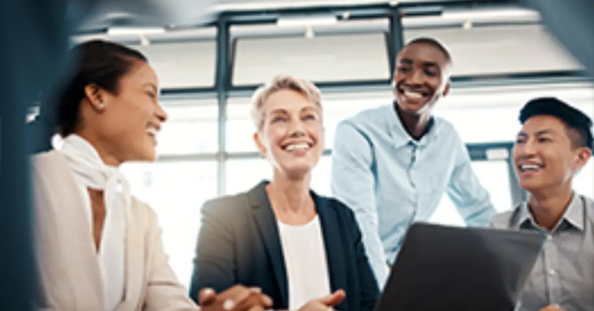 A group of four professionals collaborate around a laptop in a modern office setting, engaged in a productive discussion.